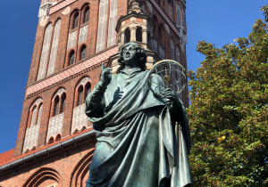 Pomnik Mikołaja Kopernika w Toruniu. Za nim stoi wykonany z czerwonej cegły Ratusz Staromiejski.
